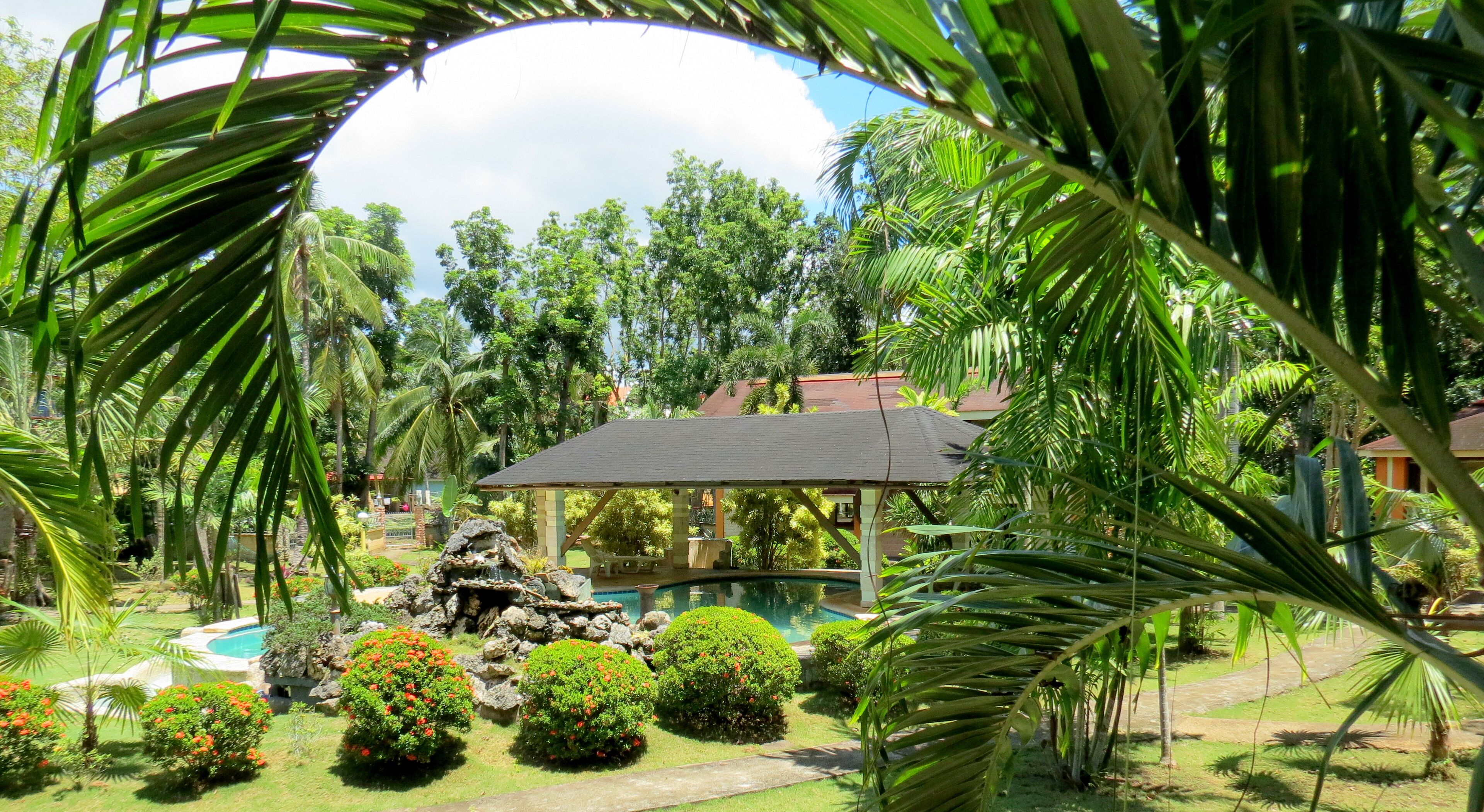 Un jardín tropical con piscina, un pabellón y una fuente de piedra.