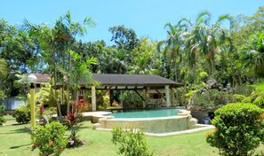 A pool area with a gazebo, surrounded by lush greenery and a clear blue sky. - Alonaland Resort Apartelle (Panglao)