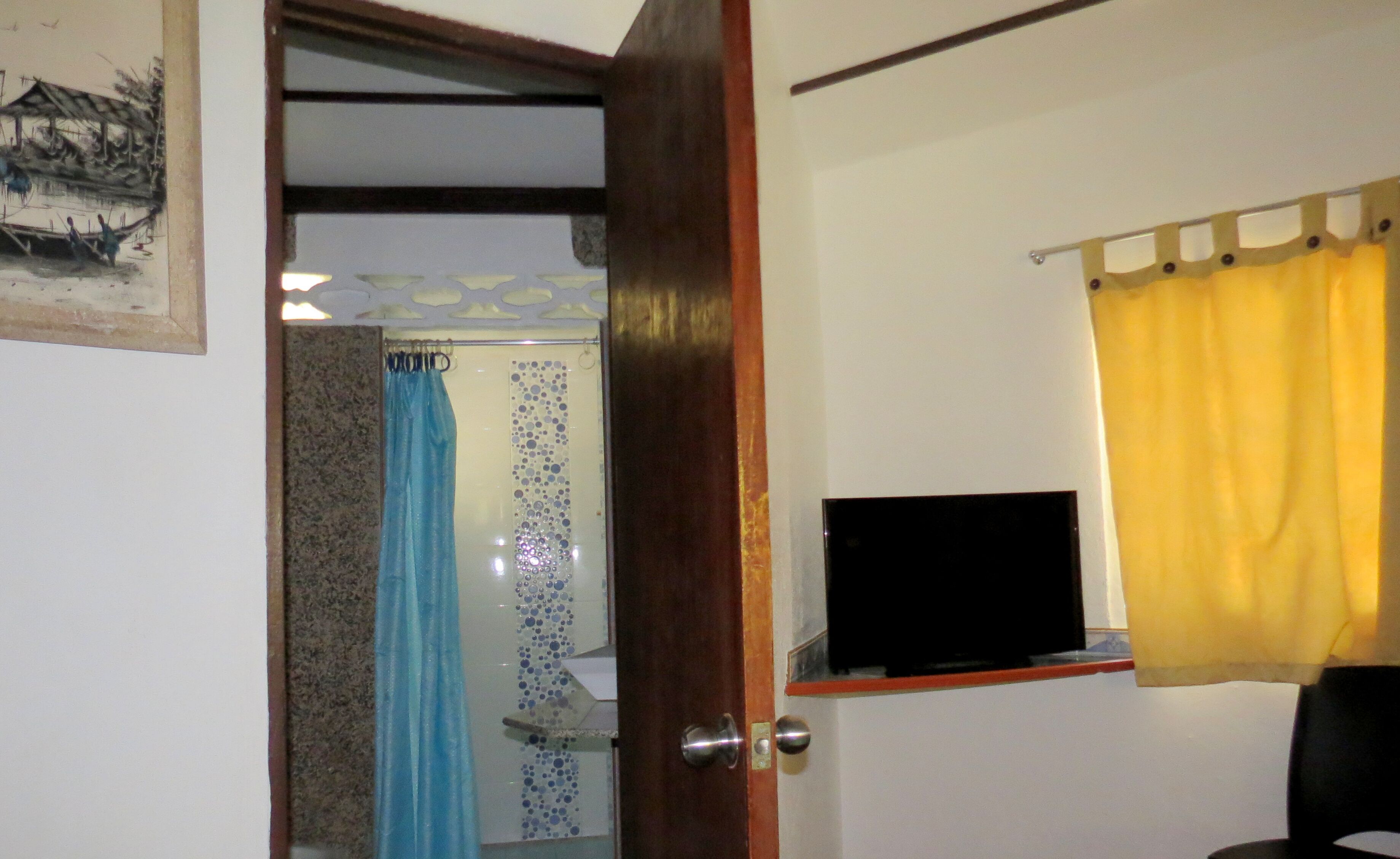 Una habitació amb una porta de fusta, una televisió sobre una prestatgeria, una cortina groga i una cortina blava.