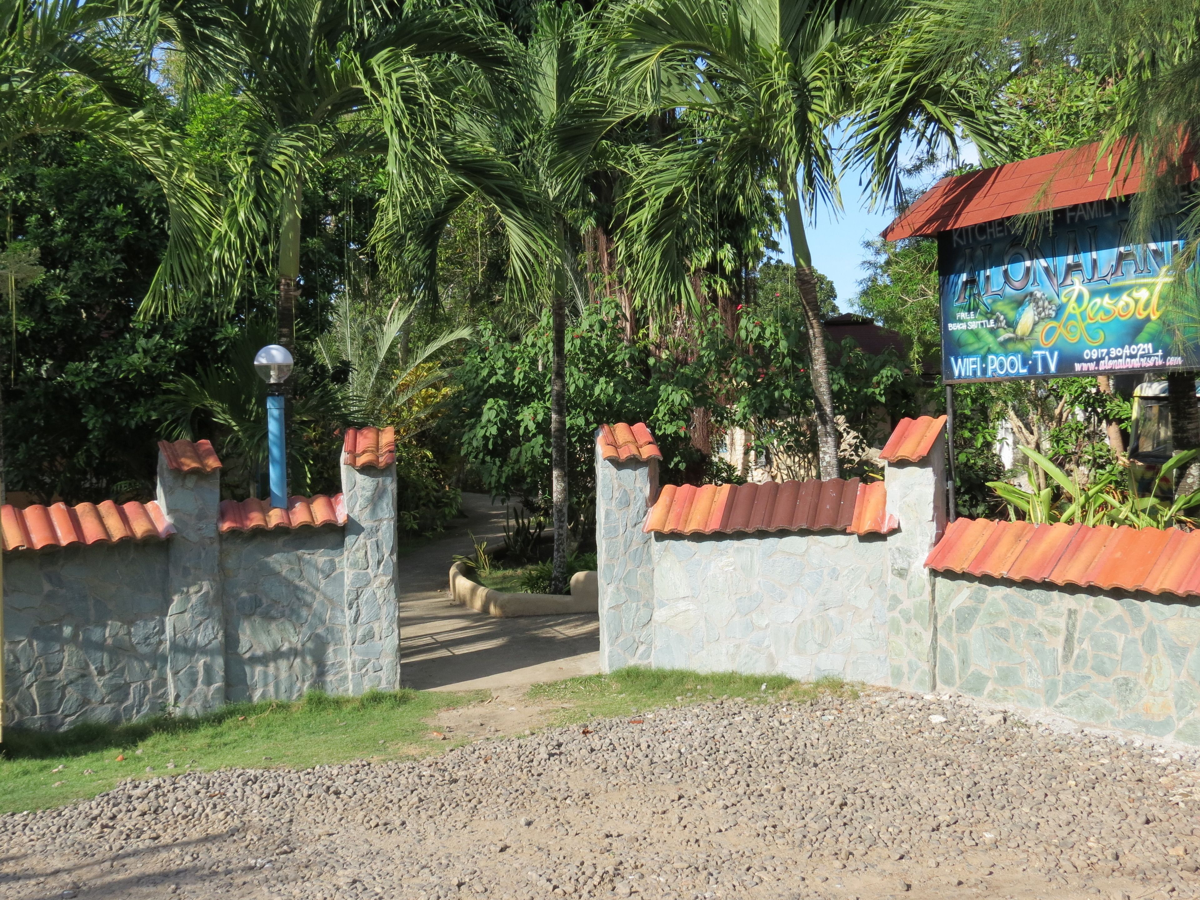 Una entrada protegida por muros de piedra y techo de tejas, que conduce a un edificio con un letrero publicitario de cocina, restaurante y ambiente familiar.