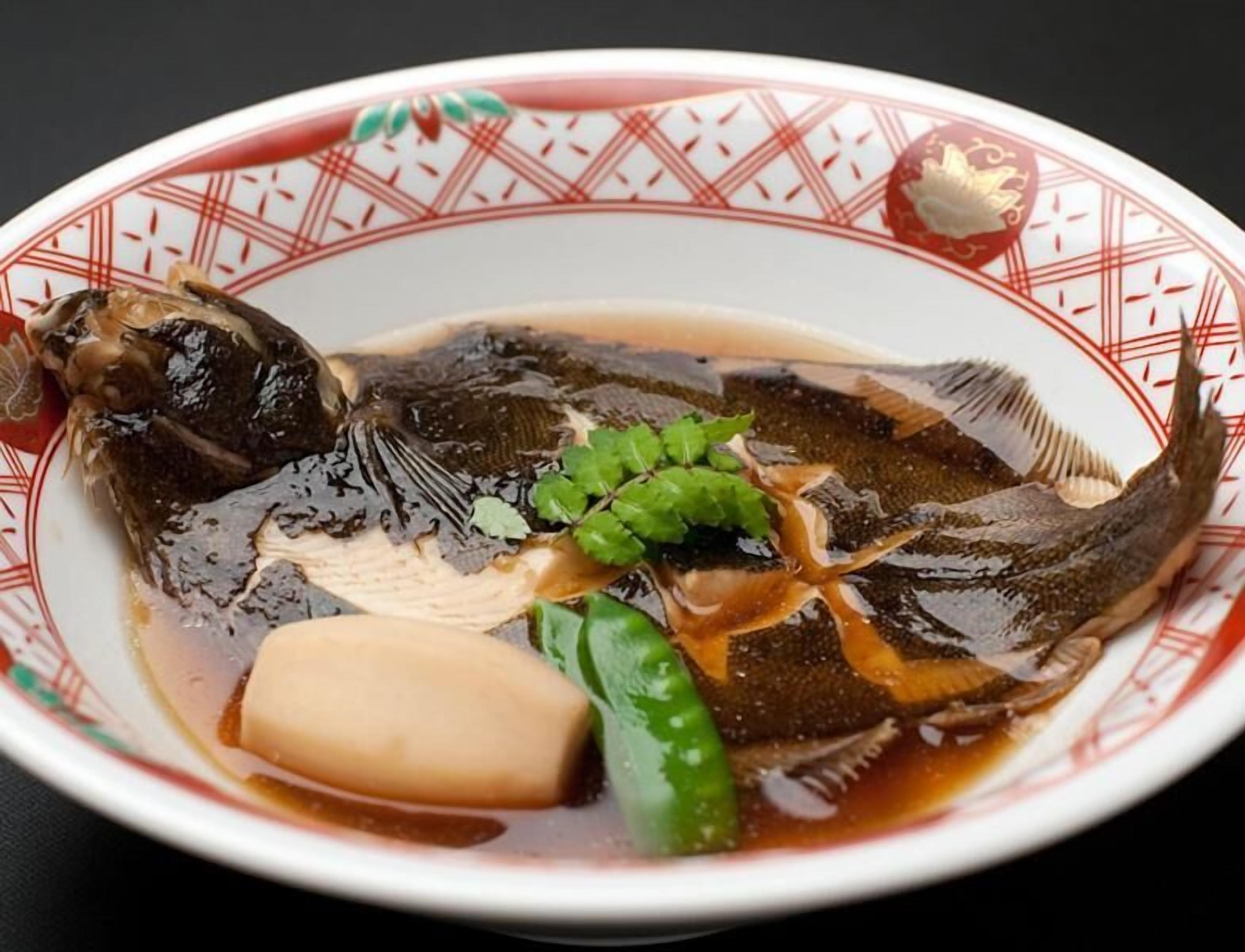 A bowl of fish soup with tofu and green vegetables.