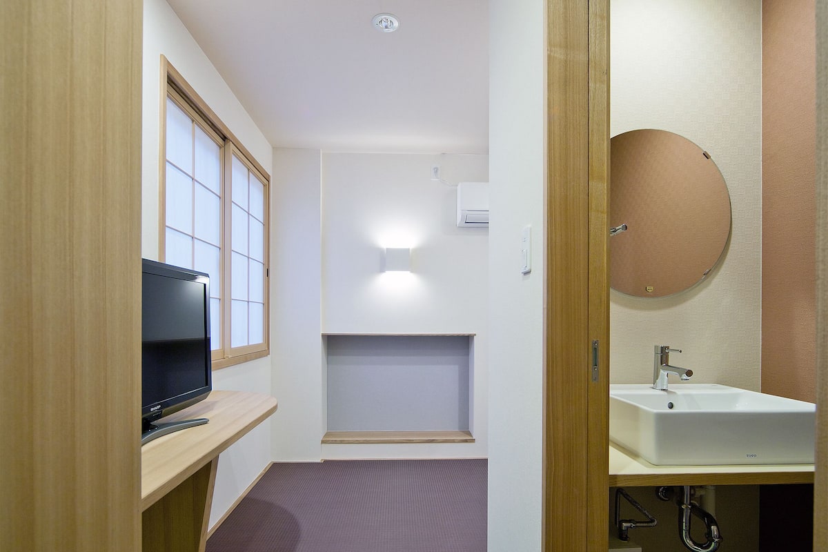 Habitación pequeña con televisión, un estante, inodoro y lavamanos.