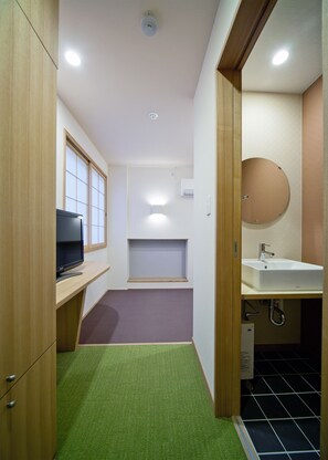 Habitación pequeña con televisión, un estante, inodoro y lavamanos.