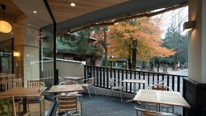 An outdoor seating area with tables and chairs, a wooden deck, and a view of trees with autumn foliage. - Ryosaino Oyado Mizuhaso (Hatsukaichi)