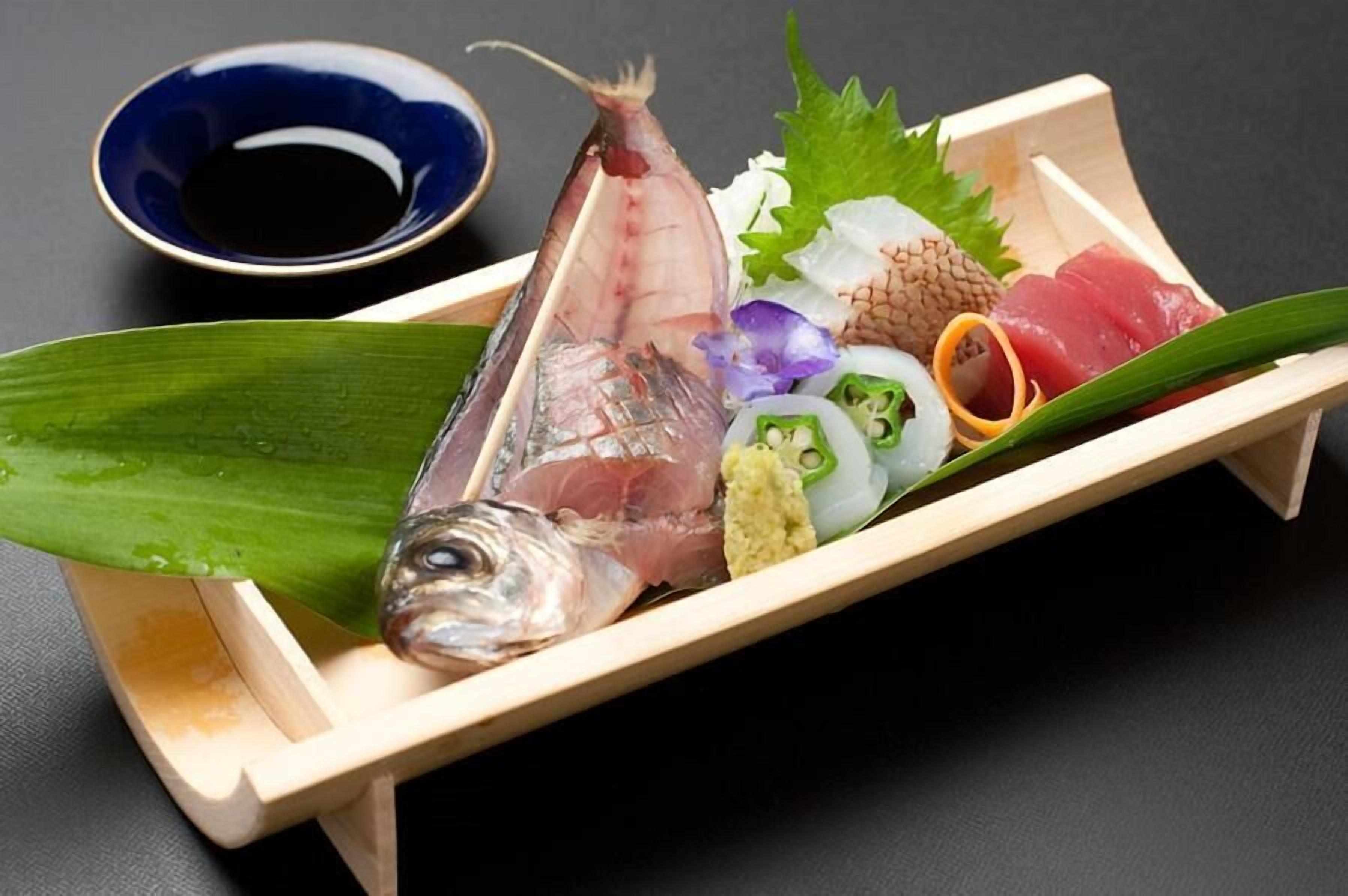 A wooden tray with various sushi pieces, a bowl of soy sauce, and a green leaf.