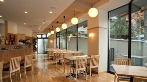 A modern restaurant interior with wooden furniture, pendant lighting, and large windows offering a view of the outdoors. - Ryosaino Oyado Mizuhaso (Hatsukaichi)