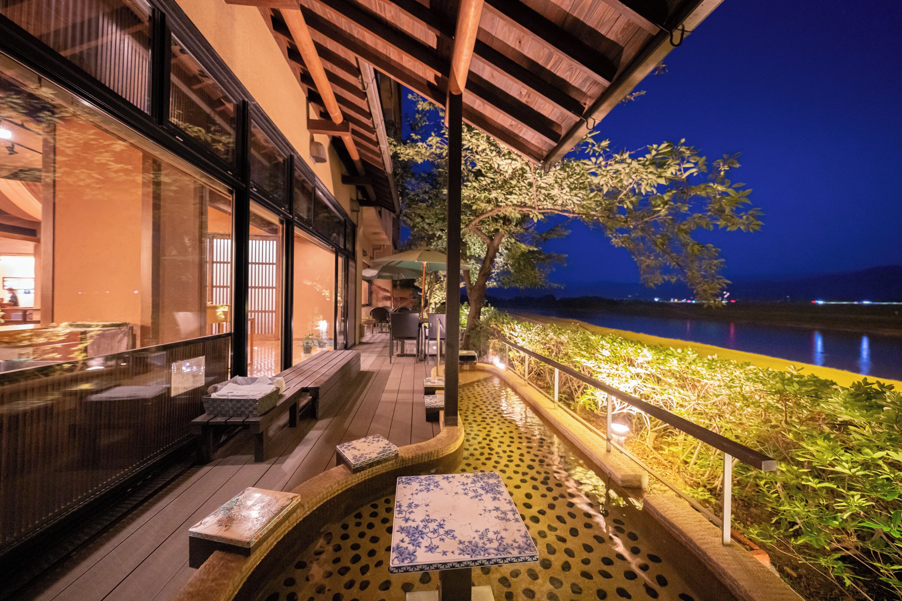 An outdoor terrace with seating, a view of a body of water, and a building with large windows.