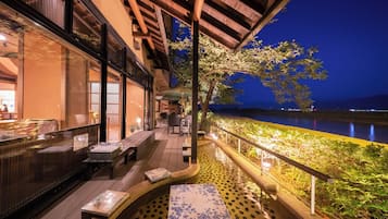 An outdoor terrace with seating, a view of a body of water, and a building with large windows.