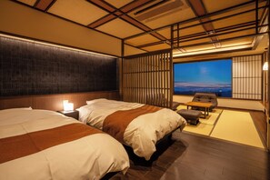 A hotel room with two beds, a nightstand, a small table, and a view of the cityscape.