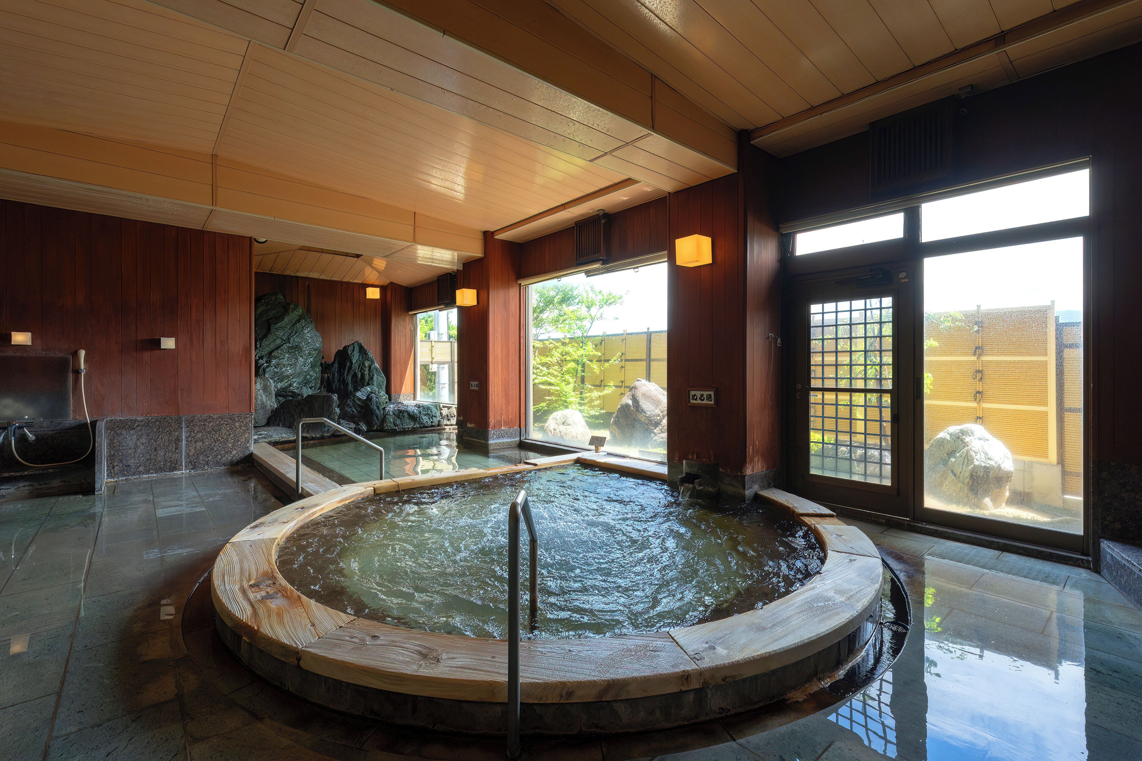 A traditional Japanese onsen with a wooden bath, stone steps, and a view of the outside.
