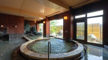 A traditional Japanese onsen with a wooden bath, stone steps, and a view of the outside.