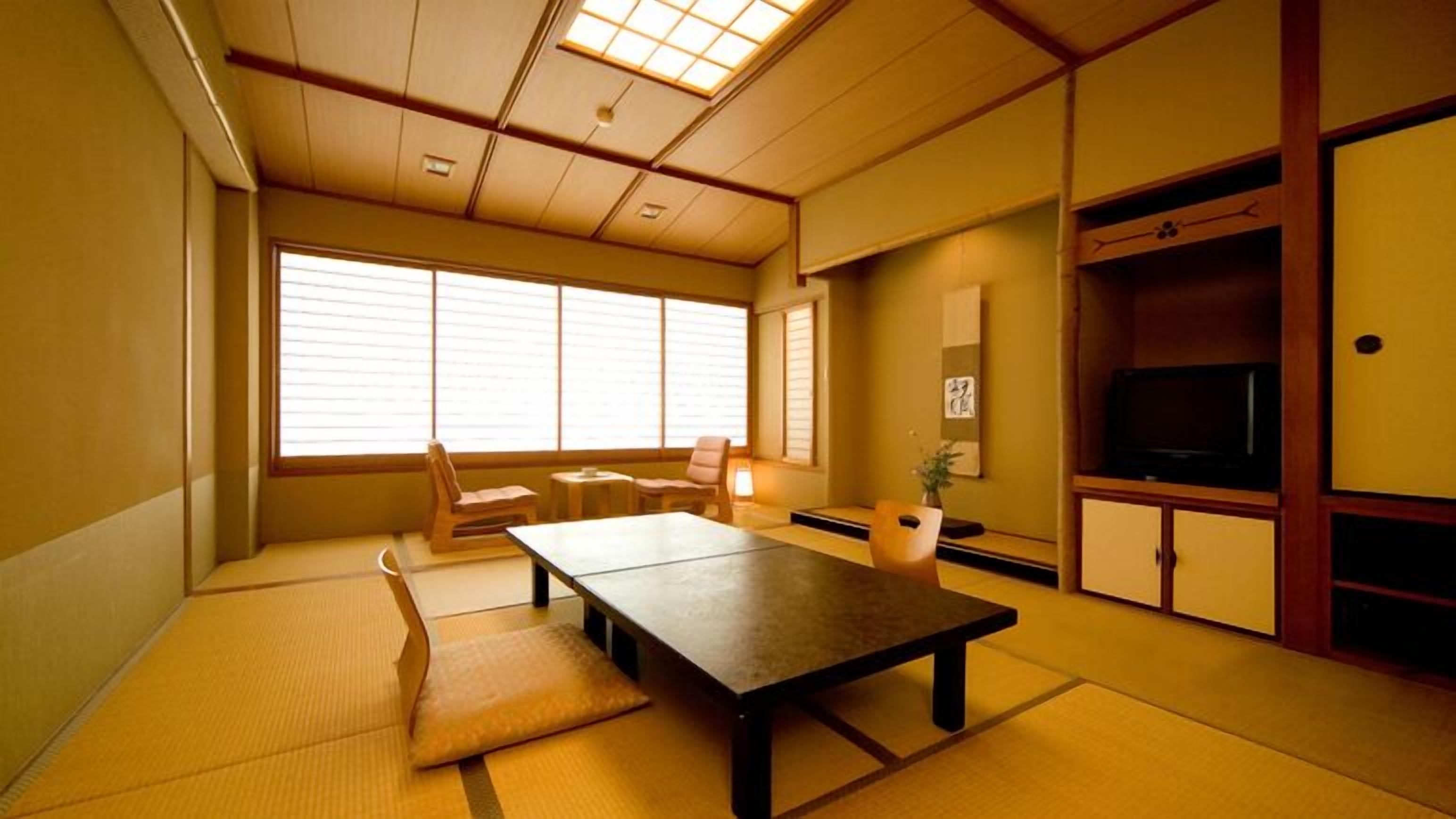 Une pièce de style japonais traditionnel, avec un sol recouvert de tatamis, une table basse, des chaises, un téléviseur et des portes coulissantes.