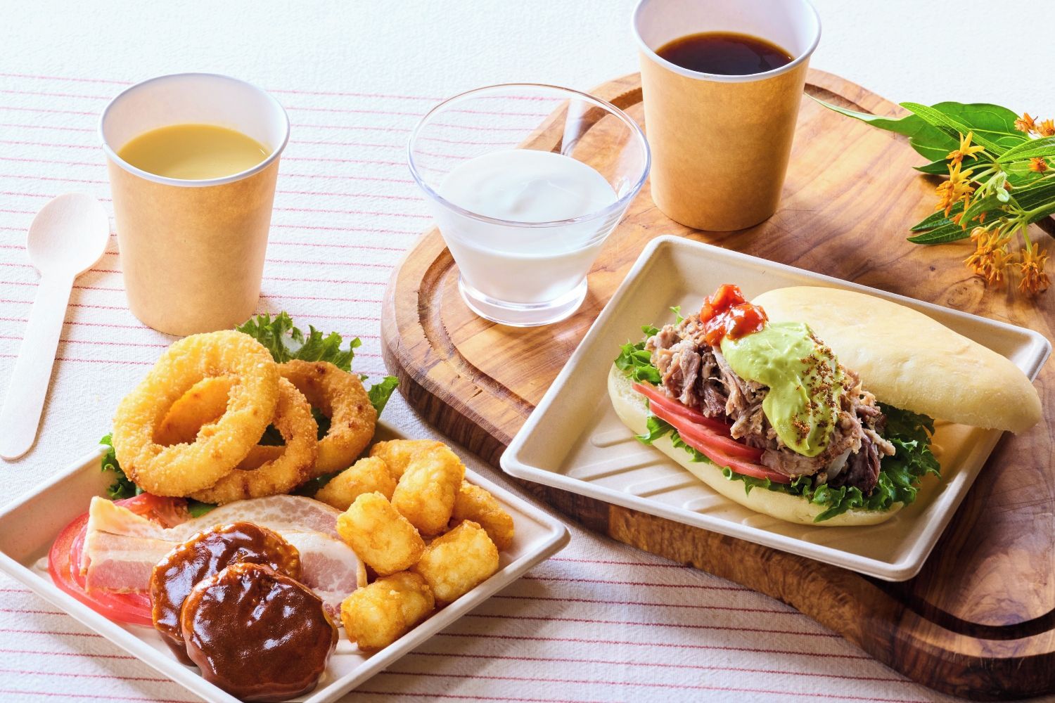 A meal with a sandwich, tater tots, onion rings, and a drink.