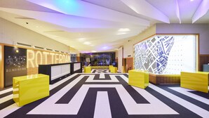 A modern hotel lobby with a geometric patterned carpet, a reception desk, and a seating area with yellow chairs. - Hotel Rotterdam Huis Ten Bosch (Sasebo)