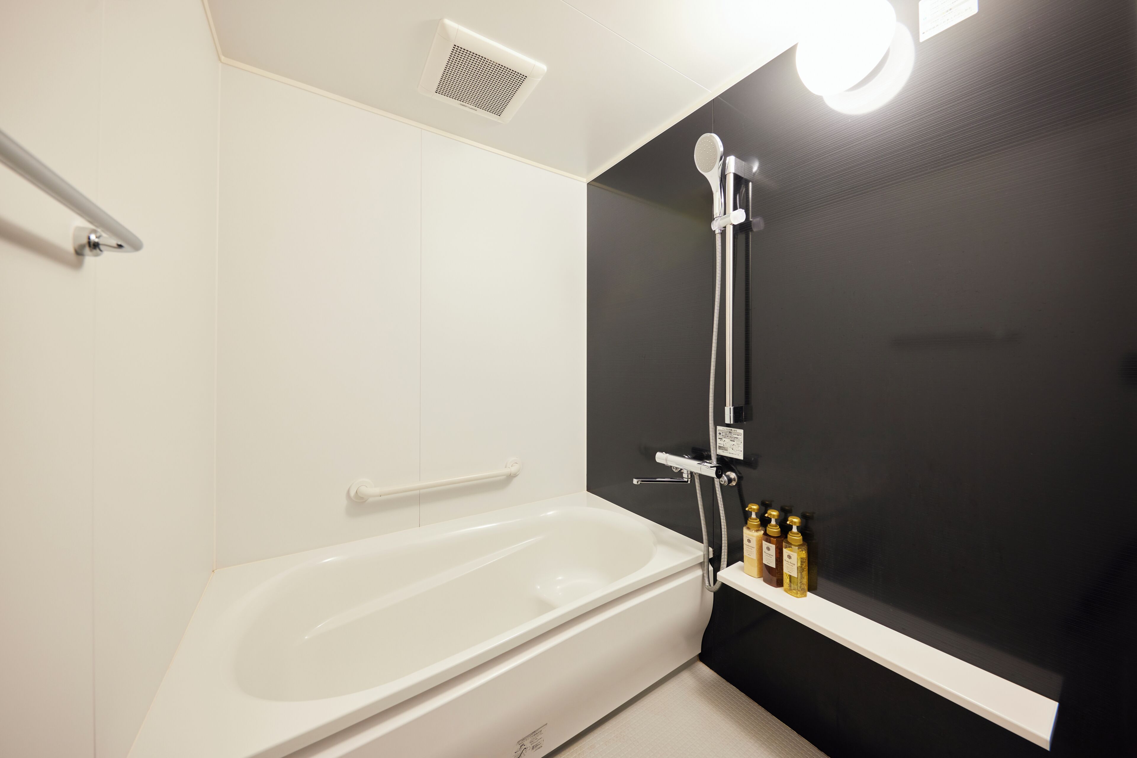A modern bathroom with a white bathtub, a showerhead, and a shelf with toiletries.