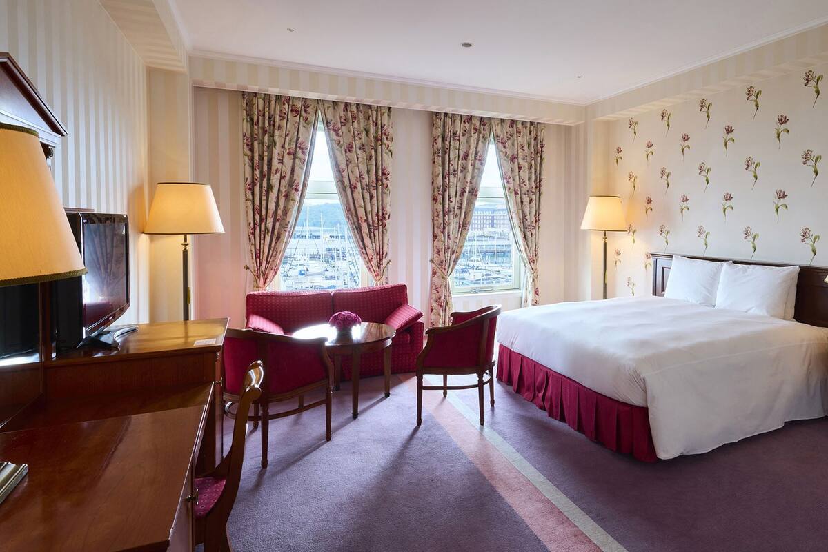 Une chambre d’hôtel comprenant un lit, deux tables de chevet avec des lampes, un bureau avec une télévision, une chaise et un canapé.