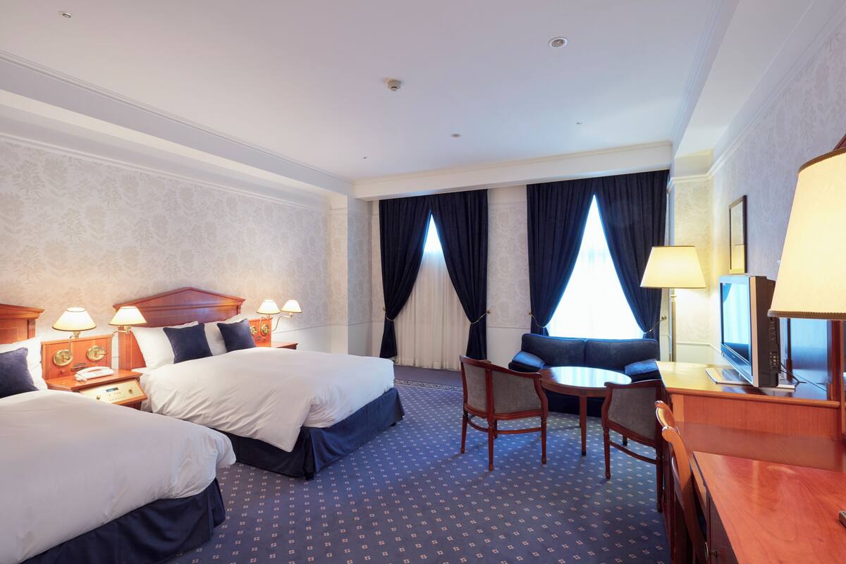 Une chambre d’hôtel avec deux lits, un bureau, une chaise, une télévision et une fenêtre avec des rideaux.