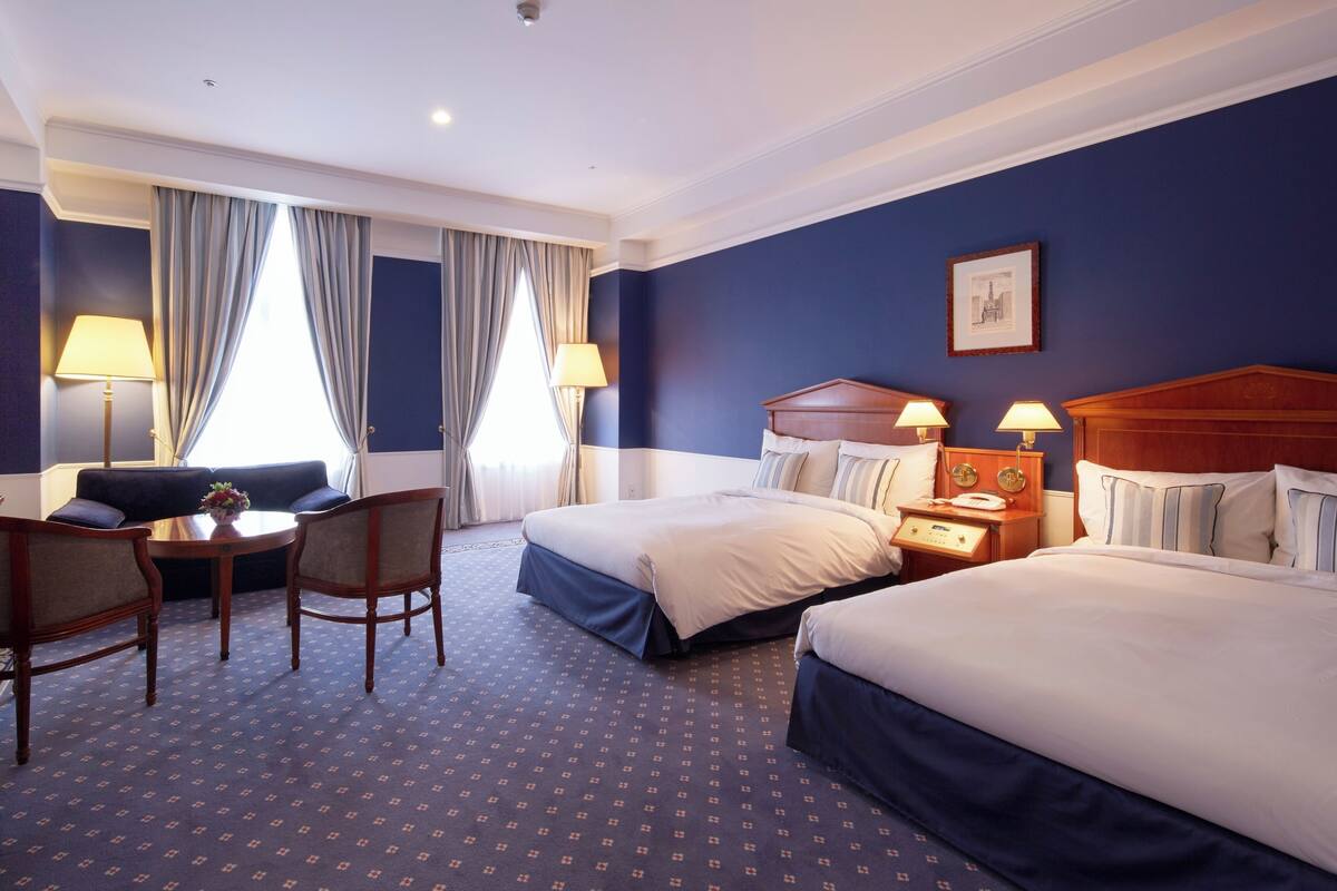 Une chambre d’hôtel avec deux lits, un canapé, une table et des lampes.
