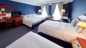 A hotel room with two beds, a desk with a television, a chair, and a small table with a lamp.