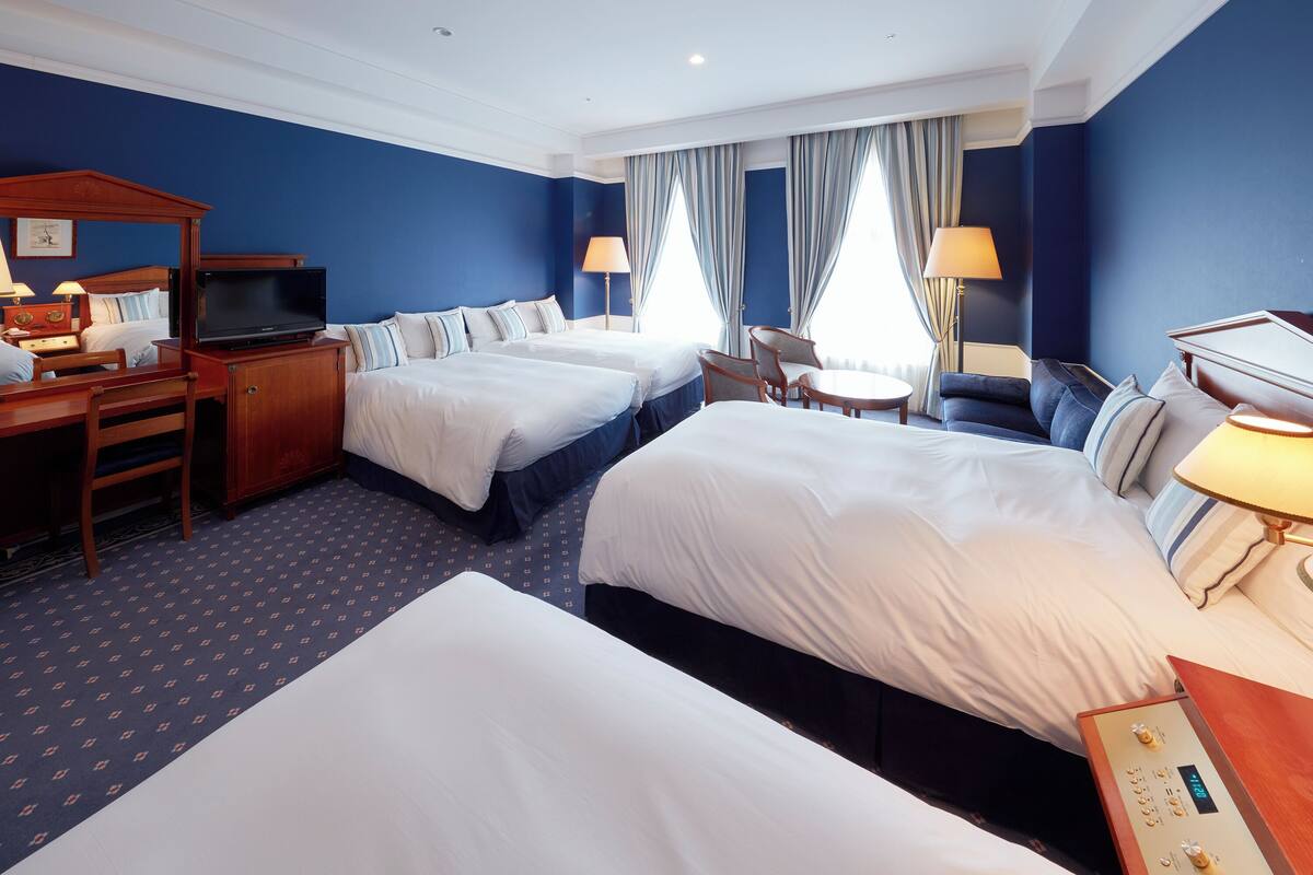 Une chambre d’hôtel avec deux lits, un bureau avec une télévision, une chaise et une petite table avec une lampe.
