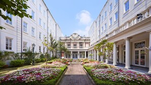 A courtyard with a central pathway flanked by flower beds and buildings with classical architecture.