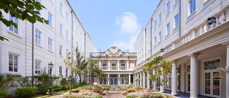 A courtyard with a central pathway flanked by flower beds and buildings with classical architecture.