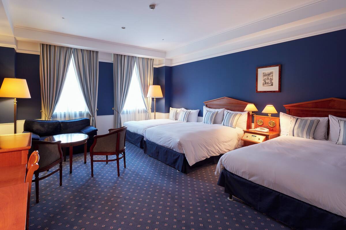 Une chambre d’hôtel avec deux lits, un canapé, un fauteuil et un bureau avec des lampes.