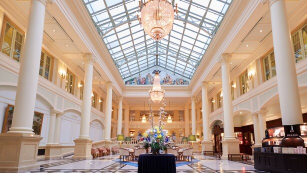 A grand lobby with a high glass ceiling, large chandeliers, and classical columns.