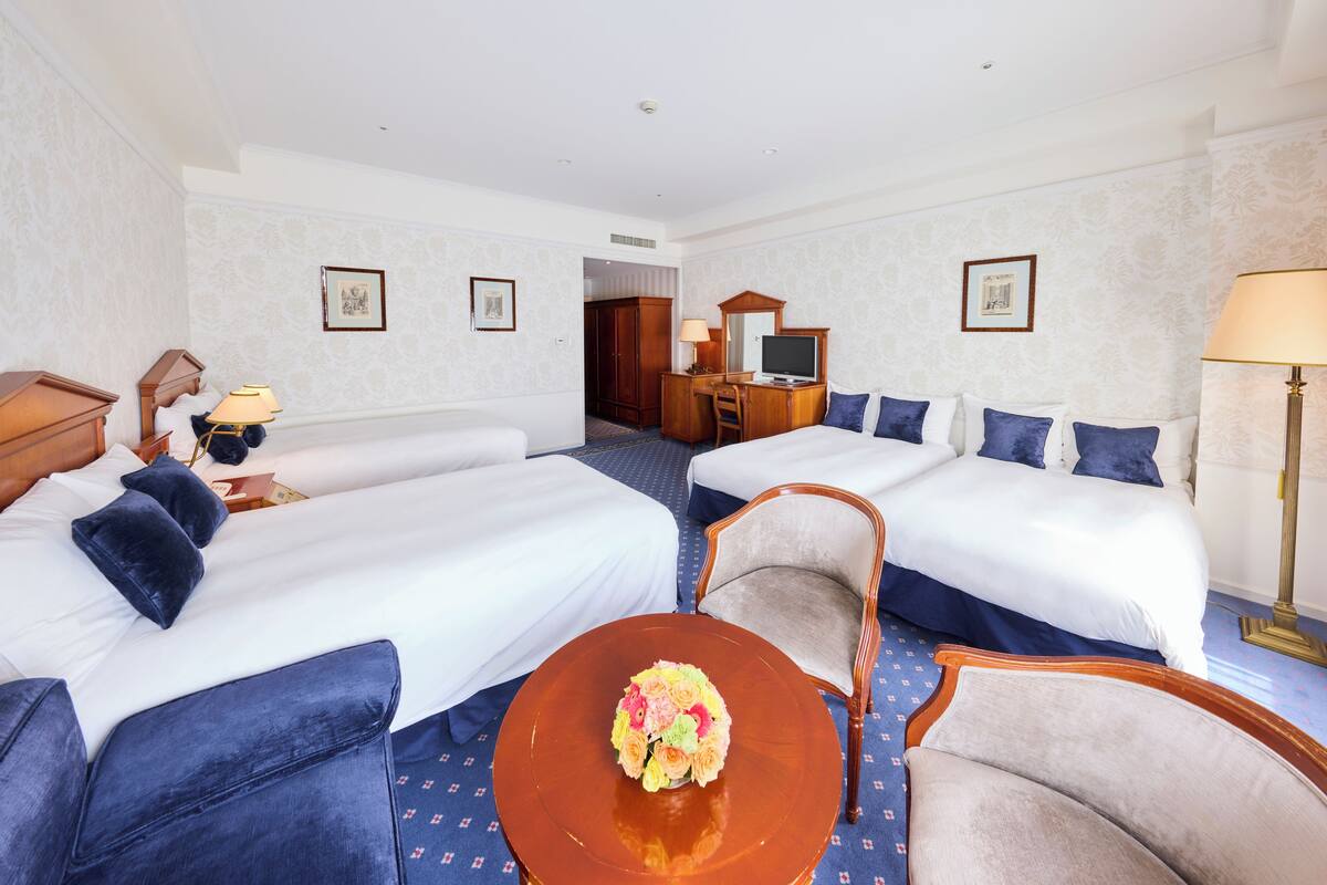 Une chambre d’hôtel avec deux lits, un bureau, une chaise et une table ronde agrémentée d’un arrangement floral.