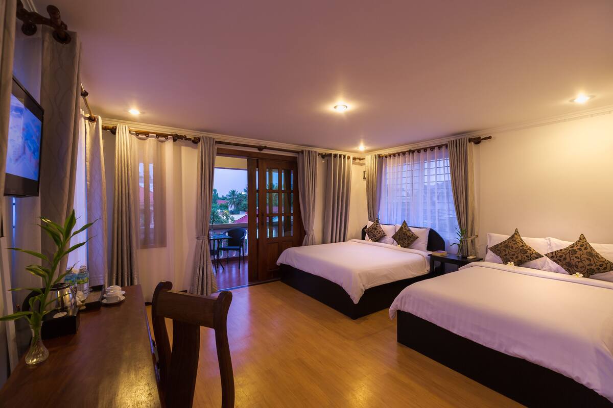 A hotel room with two beds, a dining table, chairs, a TV, and a view of the outdoors.