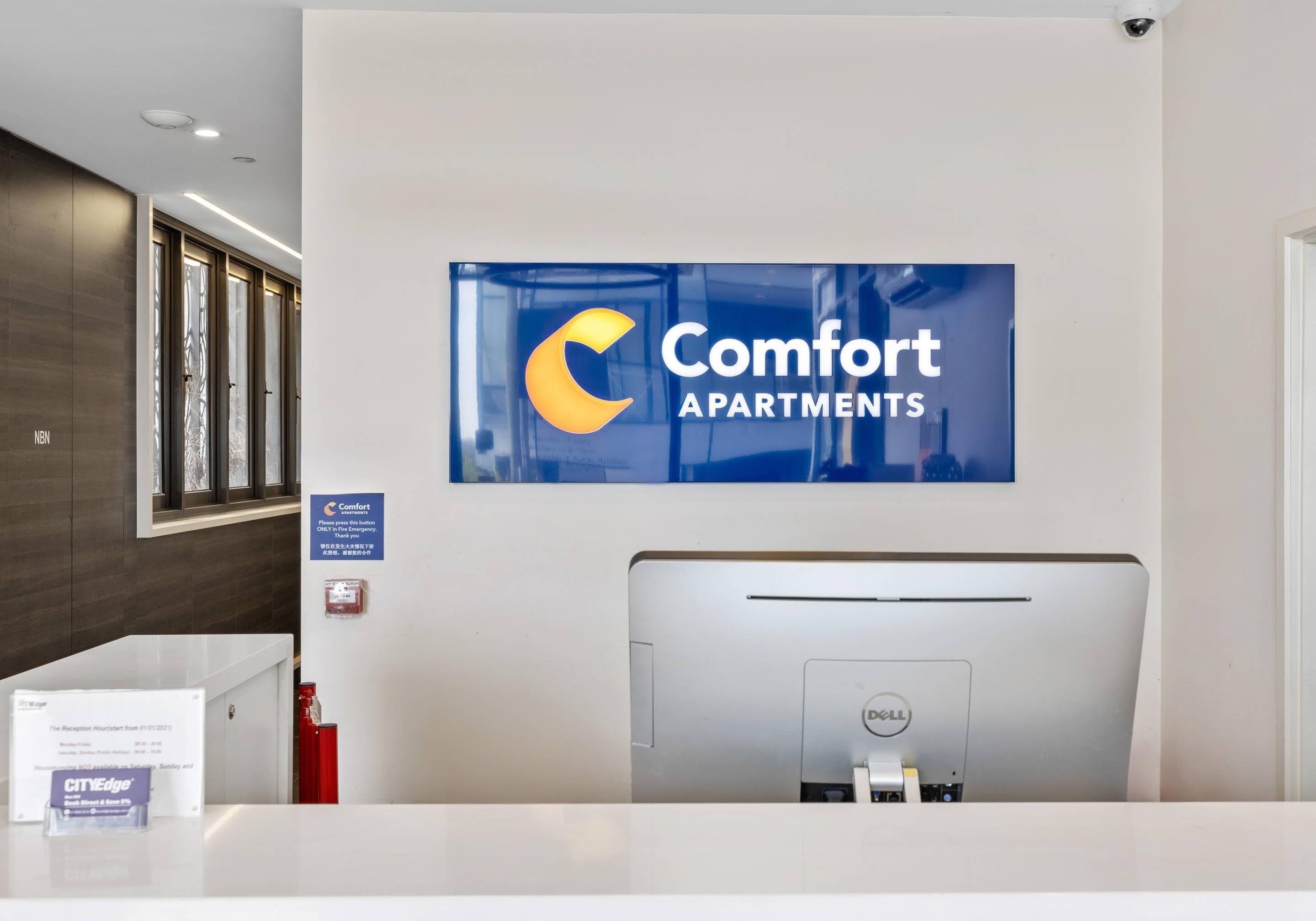 Un mostrador de recepción con un cartel de Comfort Apartments, una computadora Dell y un extintor.