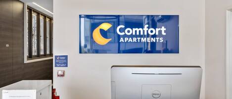 Un mostrador de recepción con un cartel de Comfort Apartments, una computadora Dell y un extintor.