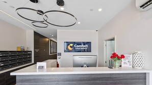 A reception desk with a sign for Comfort Apartments, a Dell computer, a visitor voucher, and a vase with red flowers. - Comfort Apartments Box Hill (Box Hill)