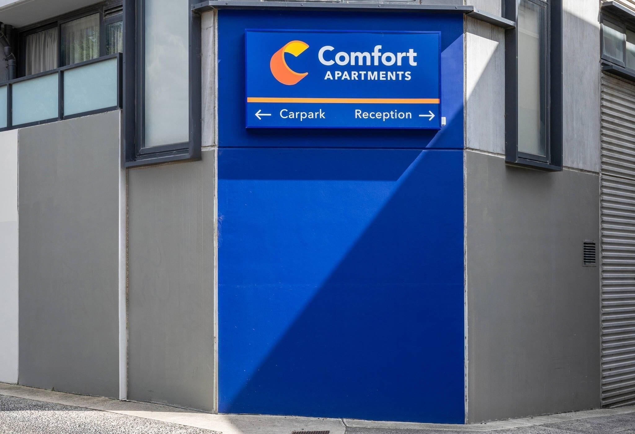 Sininen opastekyltti, jossa lukee »Comfort Apartments» ja on nuolimerkit, jotka osoittavat pysäköintialueelle ja vastaanottoon.