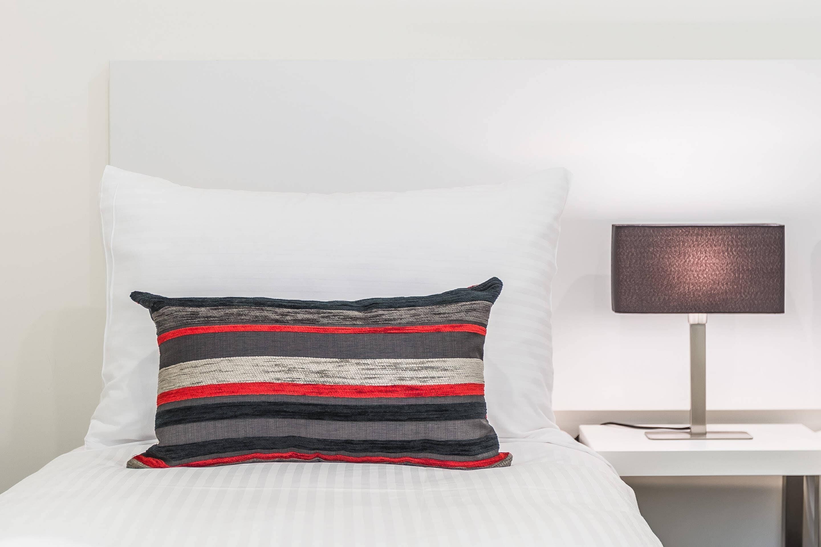 A bed with white bedding, a striped pillow, and a bedside table with a lamp.