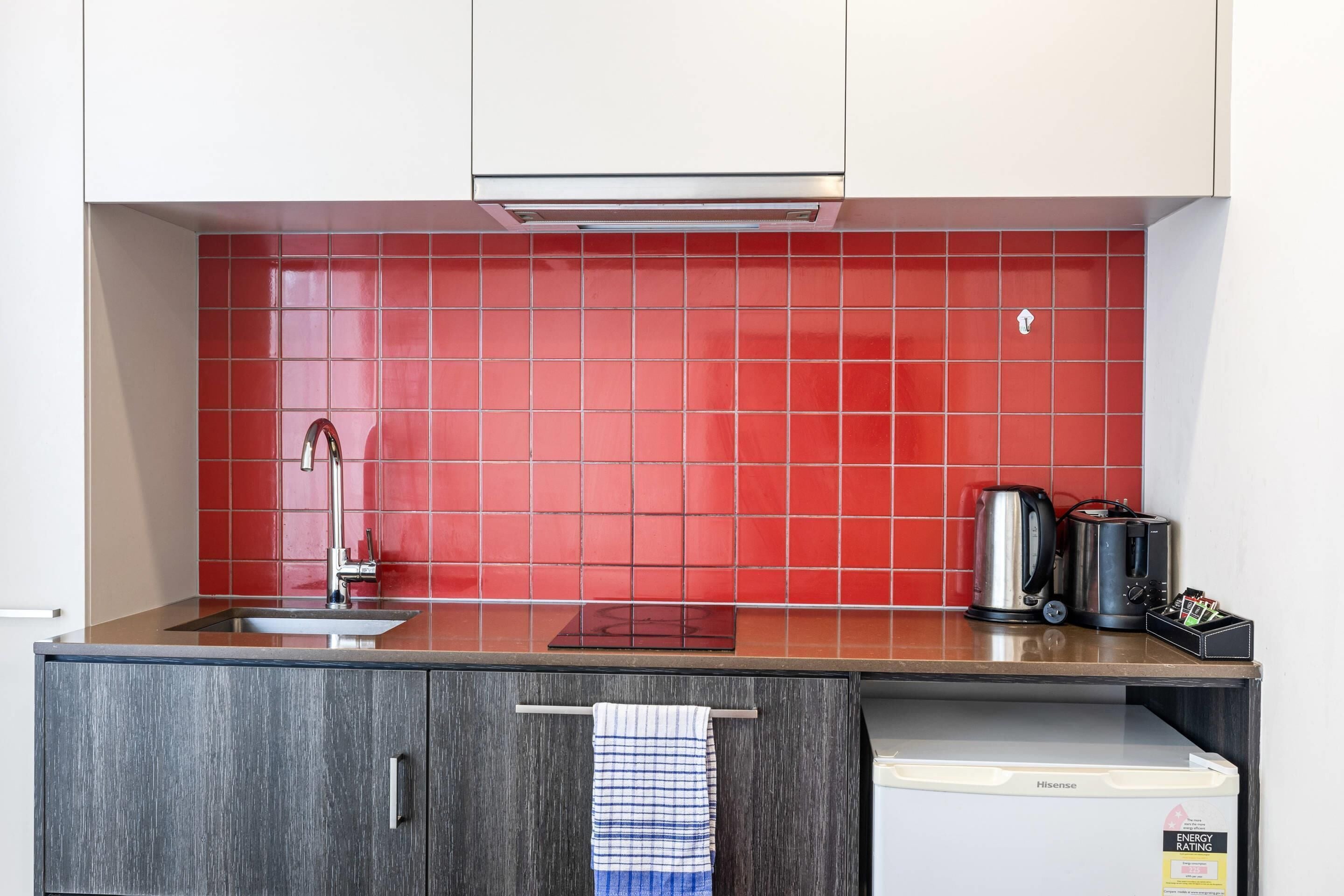 A kitchen with a red tiled backsplash, stainless steel appliances, a sink, and a Hisense refrigerator.