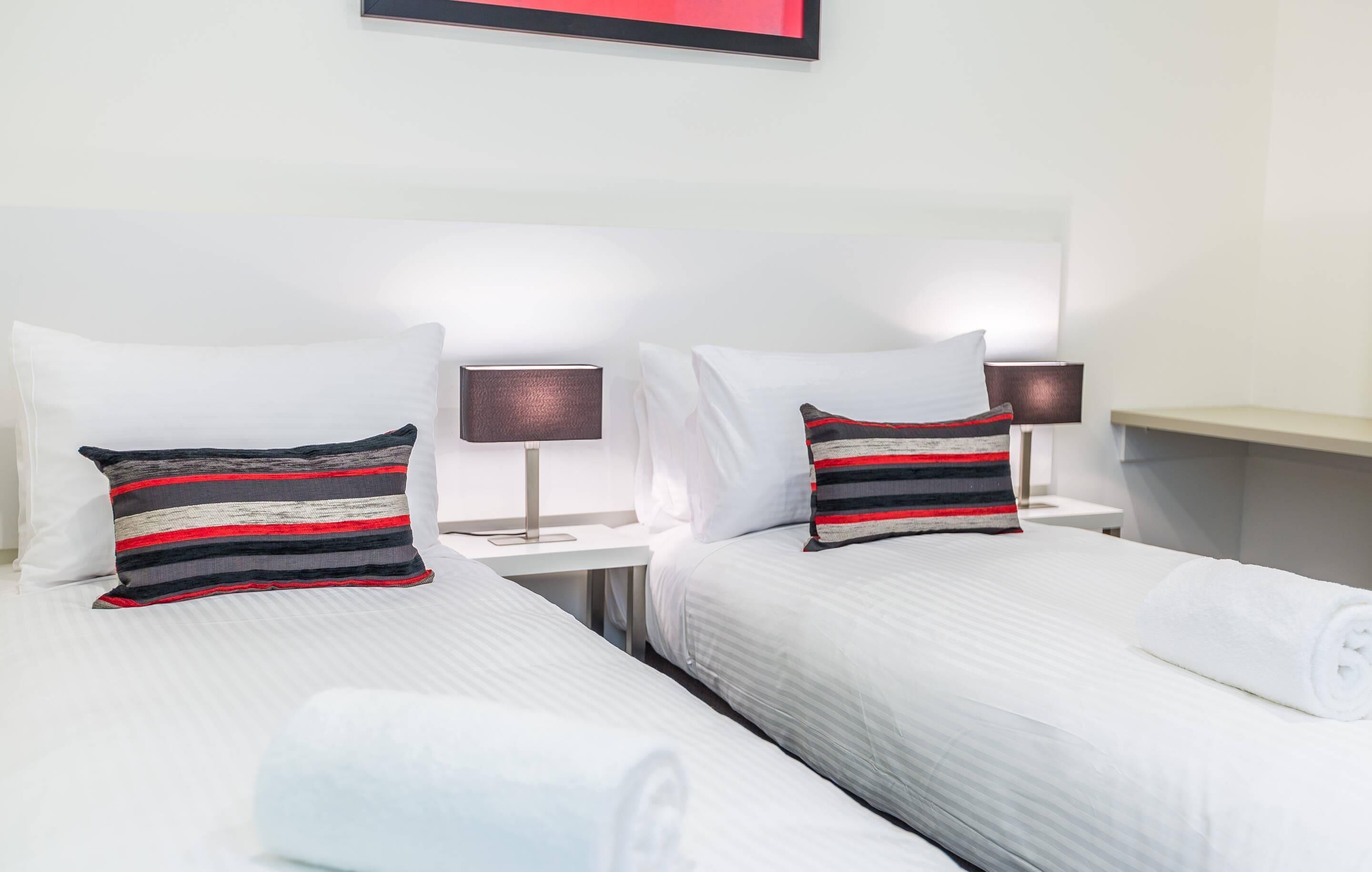 A hotel room with two beds, white bedding, striped pillows, bedside lamps, and a framed picture on the wall.