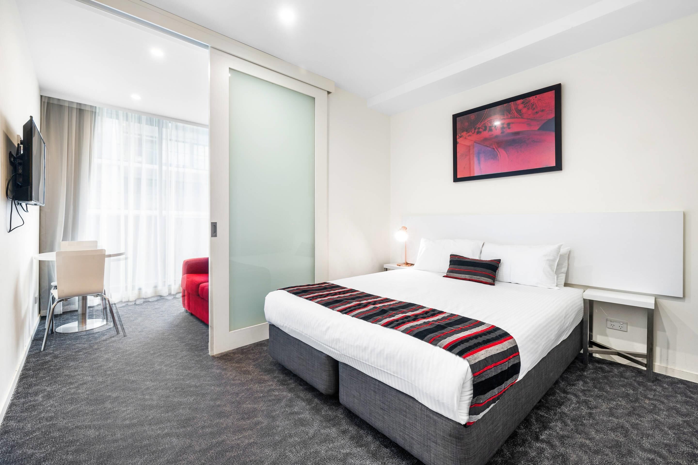 Une chambre d’hôtel avec un lit, une télévision, un bureau et une chaise rouge.