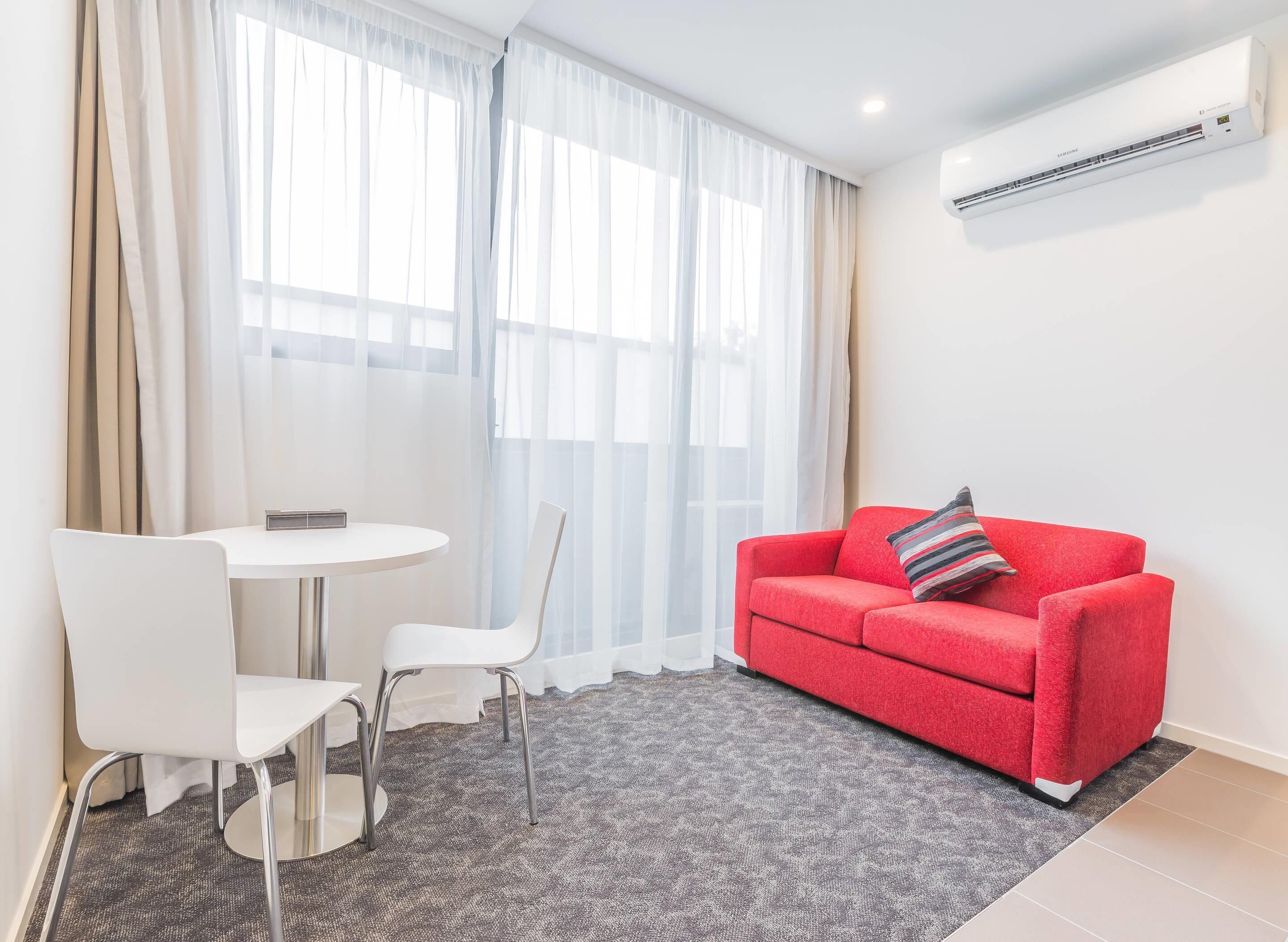 A modern room with a dining table, two chairs, a red sofa, and an air conditioning unit.