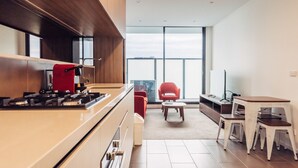 A modern kitchen with a gas stove, wooden cabinets, and a large window offering a city view. - Comfort Apartments Box Hill (Box Hill)