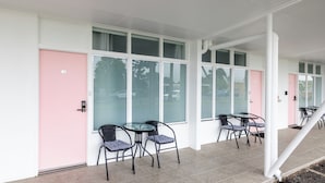 Un bâtiment doté de grandes fenêtres, d’une porte rose et d’un espace extérieur aménagé avec des chaises et des tables.