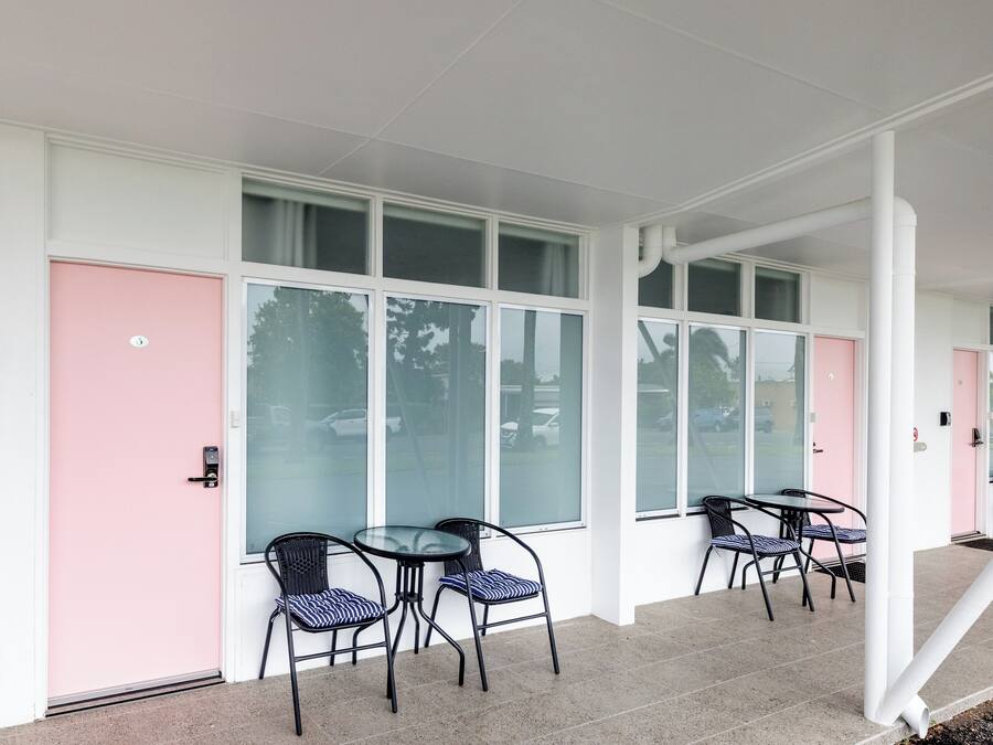 A building with large windows, a pink door, and outdoor seating with chairs and tables.