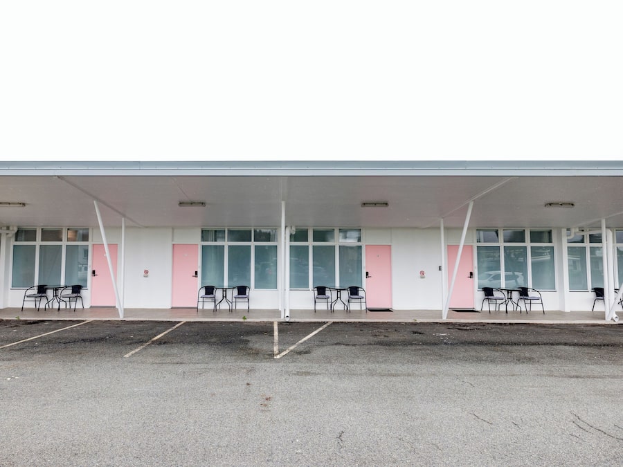 Un edificio con zona de estar al aire libre techada, varias ventanas y un estacionamiento.