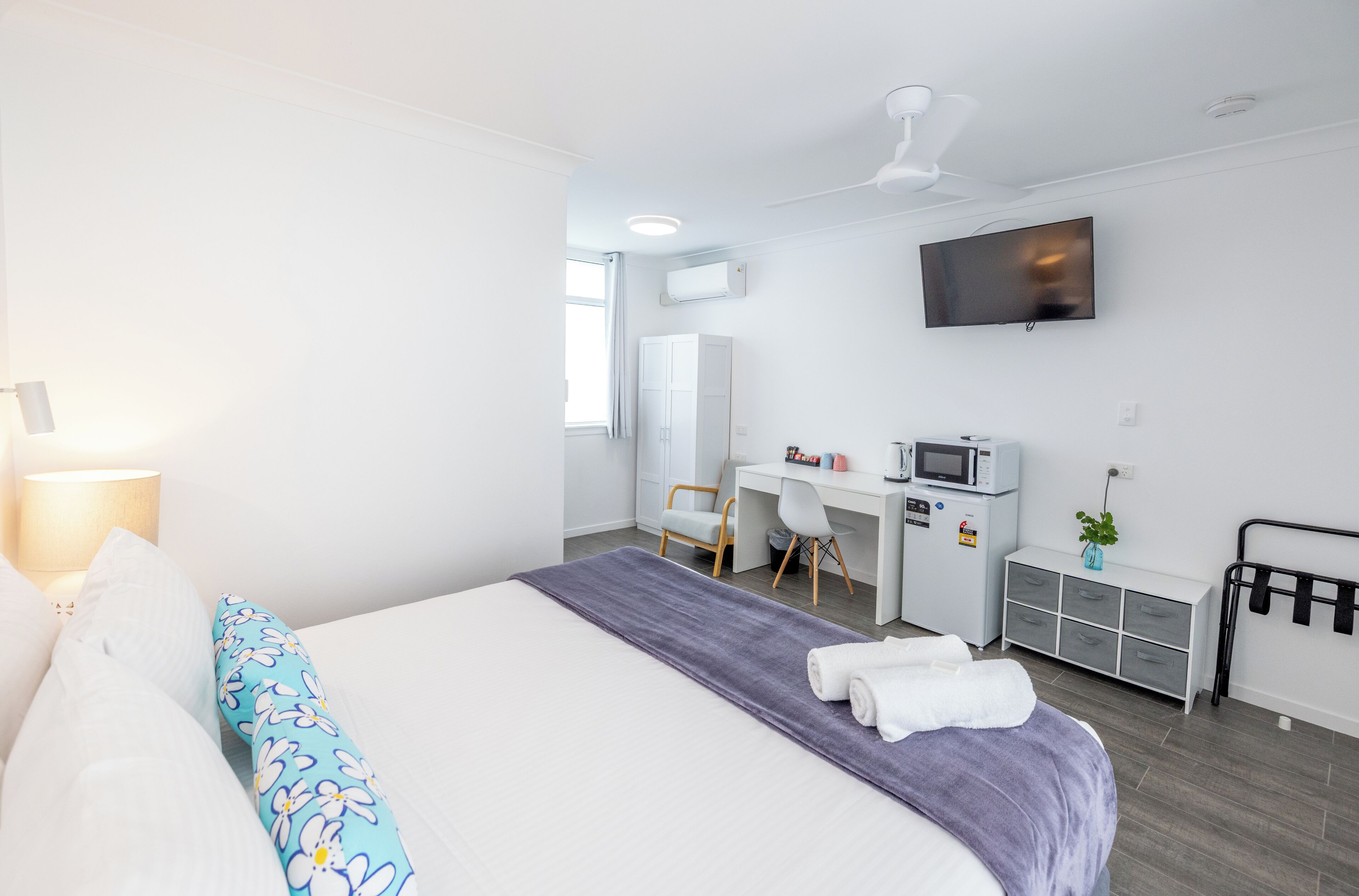 Habitación de hotel con cama, escritorio, silla, televisor y pequeña kitchenette.