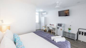 Habitación de hotel con cama, escritorio, silla, televisor y pequeña kitchenette.