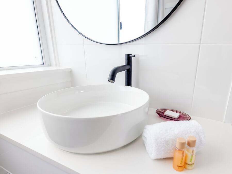 Une salle de bain avec un lavabo blanc, un miroir rond et une fenêtre.