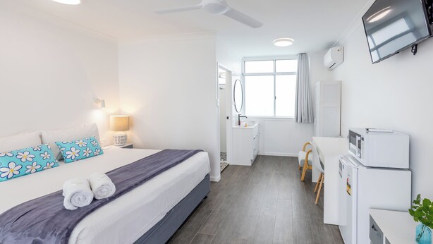 Une chambre d’hôtel avec un lit, un bureau, un miroir, une télévision et une fenêtre.