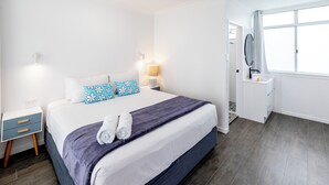 Une chambre d’hôtel moderne avec un grand lit, une table de chevet, une commode, un miroir et une fenêtre.