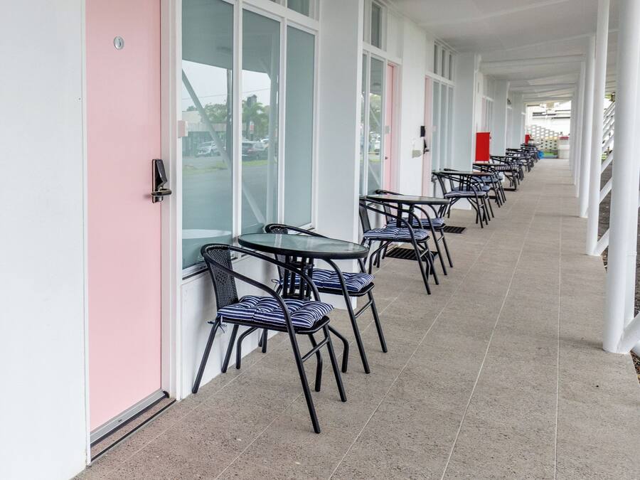 A covered corridor with tables and chairs, a pink door, and large windows.