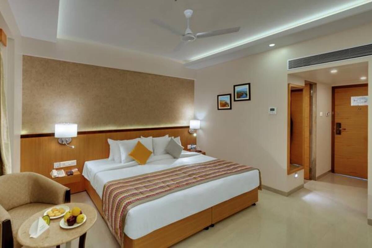 A hotel room with a bed, bedside lamps, a chair with a table, and a ceiling fan.